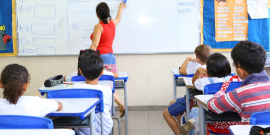 sala de aula da educação infantil. alunos ocupam seus lugares. Professora escreve no quadro.