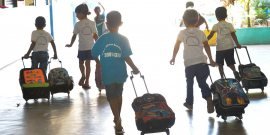 crianças de uniforme e mochilas chegando para aula, vistas de costas