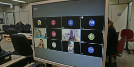 Monitor de computador exibe convidados em videoconferência. Ao fundo, cadeiras do Plenário Helvécio Arantes, vazias