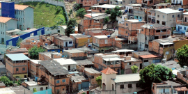 Foto do Aglomerado da Serra, durante o dia, com mais de 30 residências simples sobre área em declive.