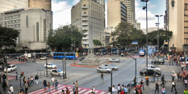 Vista aérea da Praça Sete, com pessoas e carros transitando, durante o dia. 