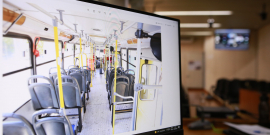 tela de computador, em primeiro plano, mostra interior de um ônibus; ao fundo, mobília do Plenário Camil Caram 