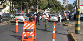 Dois agentes da BHTrans, um gaurda municipal e dois agentes sanitários realizam blitz educativa em dois carros, em rua com cones e sinalização, durante o dia