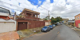 Foto de rua residencial, com mão dupla, casas e  cinco carros estacionados à esquerda, durante o dia