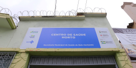 Fachada do Centro de Saúde Horto. Uma placa azul fixada ao alto da entra traz os dizeres : Centro de Saúde Horto