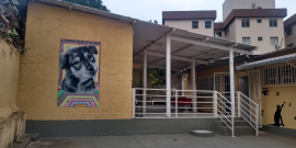 Parte interna do Centro de Esterilização de Cães e Gatos do Bairro Eplanada, com fachada amareça com a ilustração de um cão à esquerda e escada cinza com corrimão branco à direita.