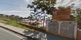 Terreno com grade e muro com placa com os seguintes dizeres: Caei - Centro de Apoio a Escola Integrada. Ao fundo, tenhado de residência, durante o dia. 