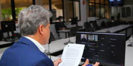 Sentado à mesa, vereador participa de reunião remota, se comunicando com outras pessoas na tela do computador.