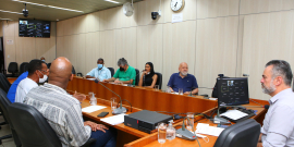 Sete homens e uma mulher reunidos, sentados à mesa.