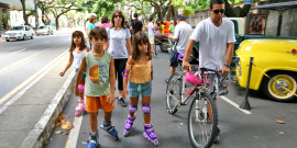 Crianças brincam de patins ao lado de um adulto com uma bicicleta