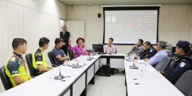 Oito homens e uma mulher sentados à mesa em reunião. 