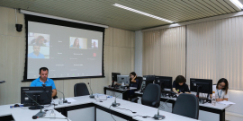 Vereador, sentado à mesa, participal de reunião virtual com outras três vereadoras, exibidas em telão.  