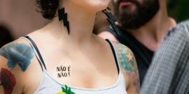 Detalhe de colo com os dizeres "Não é não!", de mulher com camiseta, entre outras pessoas, durante o dia.