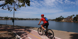 Homem anda de bicicleta em ciclovia da orla da Lagoa da Pampulha, durante o dia. 