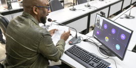 Vereador, sentado à mesa, olha a tela de computador onde sua imagem faz parte de grupo de reunião virtual, com outros quatro vereadores 