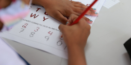 As mãos de uma criança fazendo atividade educativa: colorindo as letras pontilhadas em uma folha de ofício