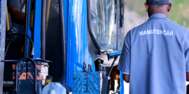 Ônibus parado ao lado de homem de camisa azul em que está escrita, nas costas, a palavra "manutenção".