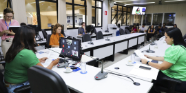 Vereadoras assentadas no Plenário Helvécio Arantes, em mesa com formato de U. O computador à frente de Loíde mostra chamada virtual e pequena plateia assiste à frente.