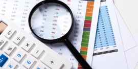 Papeis, calculadora e lupa dispostos sobre uma mesa
