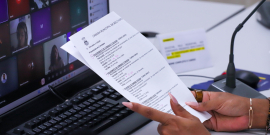 Mãos seguram documento em frente a um computador