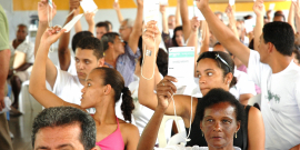 Pessoas erguem uma das mãos segurando fichas brancas em votação