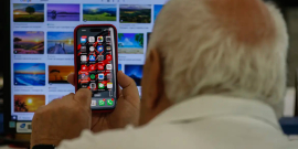 homem com o celular na mãe e o computador à frente