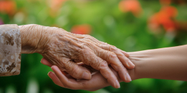Duas mãos idosas se encontram em frente a um jardim