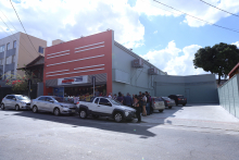 Fachada da Drograria Araújoe e estacionamento em terreno contíguo. Pintura lateral da farmácia igual à do estacionamento. Holofotes sobre a farmácia apontam para o estacionamento. Aparelhos de ar-condicionados da loja estão no estacionamento.