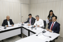 Quatro dos cinco integrantes da Comissão estão sentados ao redor da Mesa apreciando a pauta da reunião; atrás, uma coordenadora do Processo Legislativo assessora os parlamentares, 