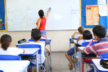 sala de aula da educação infantil. alunos ocupam seus lugares. Professora escreve no quadro.