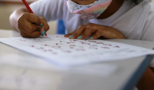 Estudante com máscara escreve em papel