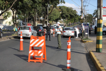 Dois agentes da BHTrans, um gaurda municipal e dois agentes sanitários realizam blitz educativa em dois carros, em rua com cones e sinalização, durante o dia