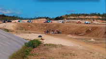 Aterro sanitário. Área de terra batida, local amplo e veículos de caçamba, entre escavadeiras e caminhões, durante o dia