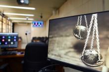 Imagem  dois pêndulos na cor prata refletida na tela do computador, fazendo alusão à balança da justiça. Ao fundo a imagem desfocada da sala de reunião
