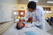 Pediatra atende bebê deitado em cama.