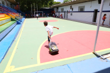 Criança com mochila atravessa pátio de escola, durante o dia. Ao fundo, outros estudantes. 