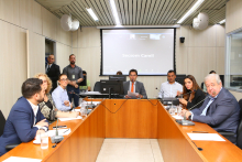 Três mulheres e quatro homens sentados à mesa em reunião. 