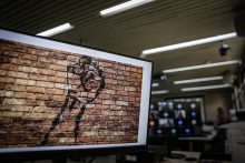 Na tela do computador a imagem de um muro de tijolinho aparente onde está desenhado uma mão com contorno preto. 