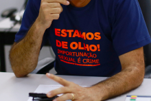 Imagem do tronco de um homem usando uma blusa azul marinho com os dizeres em vermelho: Estamos de olho! Importunação sexual é crime 