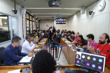 Imagem do Plenário Camil Caram lotado de participantes. Ao centro, é possível ver uma catraca de ônibus