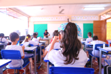 Imagem de uma sala de aula vista do fundo, os alunos estão de costa para a câmara e de frente para o quadro