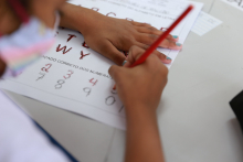 As mãos de uma criança fazendo atividade educativa: colorindo as letras pontilhadas em uma folha de ofício