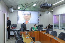 Vereador é exibido em telão de sala de reuniões, presidindo reunião de forma remota.