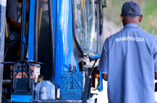 Ônibus parado ao lado de homem de camisa azul em que está escrita, nas costas, a palavra "manutenção".