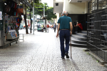 Idoso visto de costas caminha em rua de BH com bengala